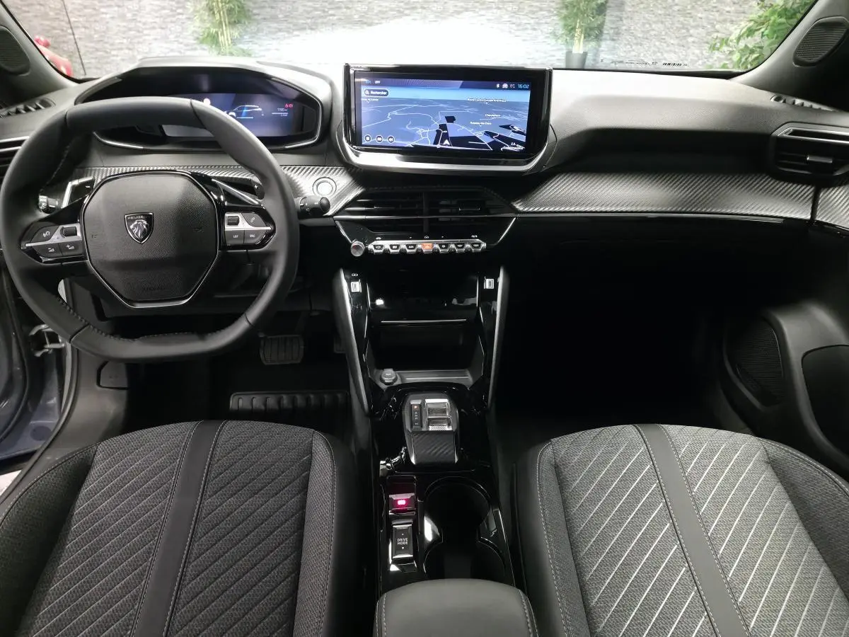 Vue intérieure avant du Peugeot 2008 1.2i Hybrid 2025, tableau de bord carbone et écran tactile central.