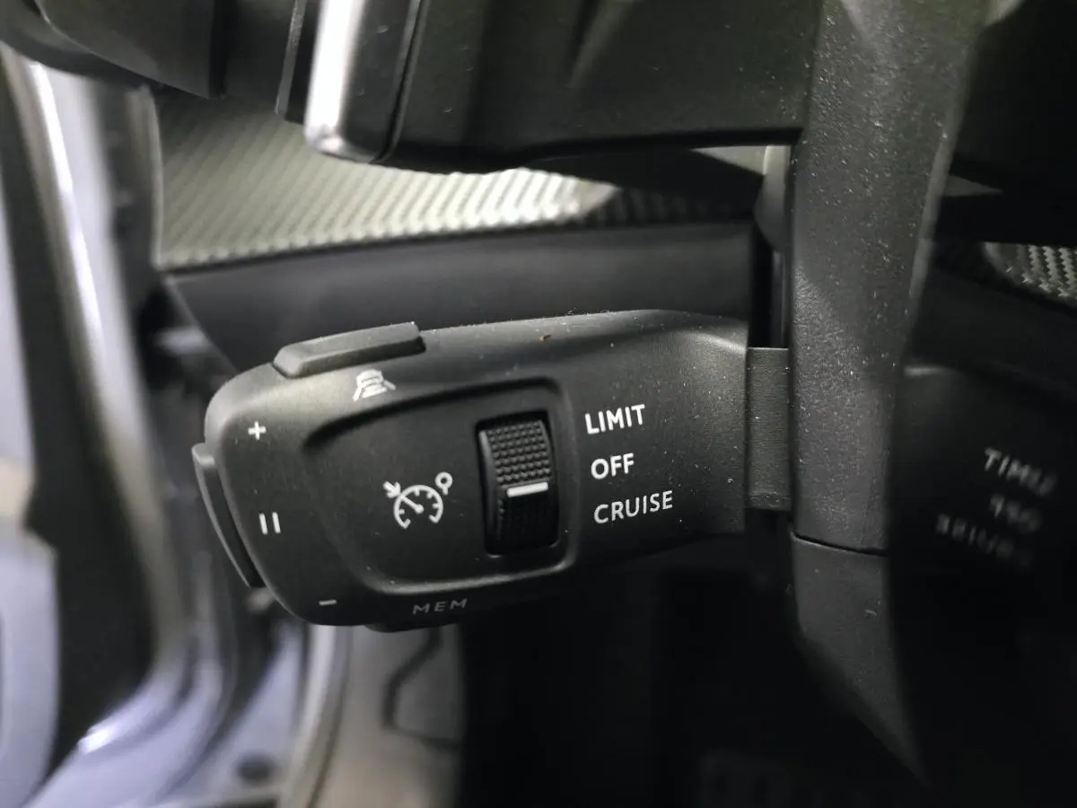 Gros plan sur la commande de régulateur de vitesse du Peugeot 2008 gris, située derrière le volant à gauche.