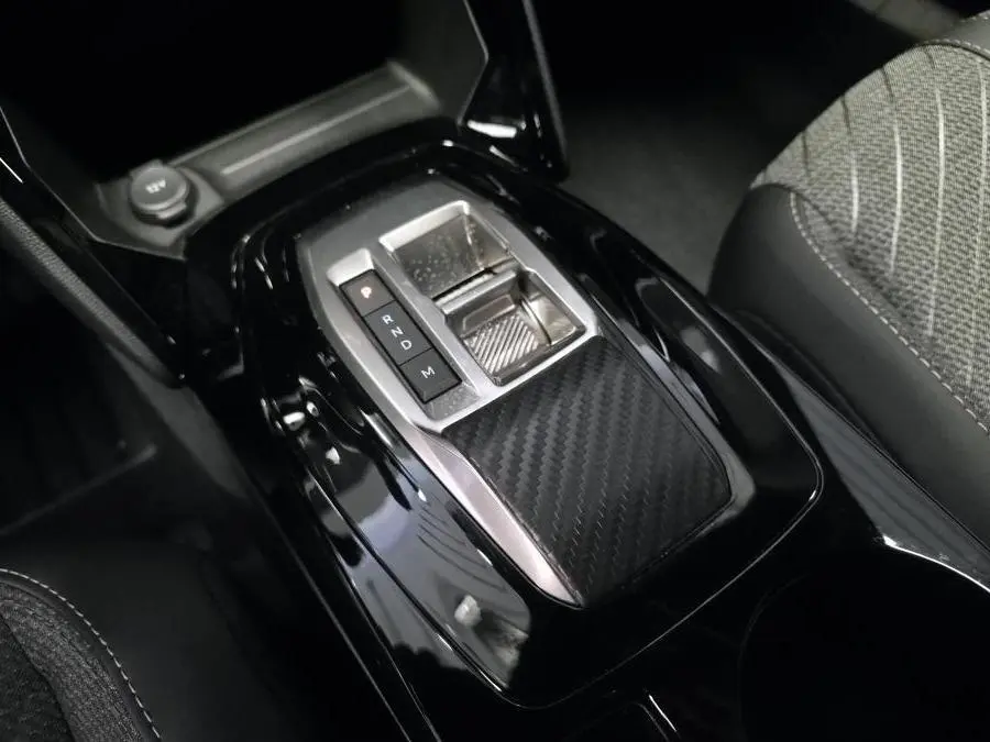Gros plan sur la console centrale noire brillante avec sélecteur de boîte automatique et décor carbone du Peugeot 2008 gris.