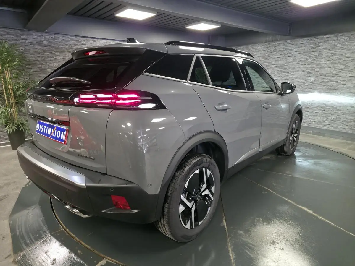 Vue 3/4 arrière droite du Peugeot 2008 gris avec toit noir et feux arrière LED allumés en intérieur showroom.