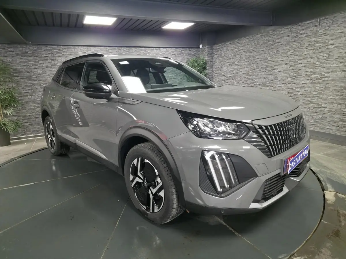 Peugeot 2008 gris en 3/4 avant droit, avec calandre noire à marquages verticaux et feux LED 3 griffes.