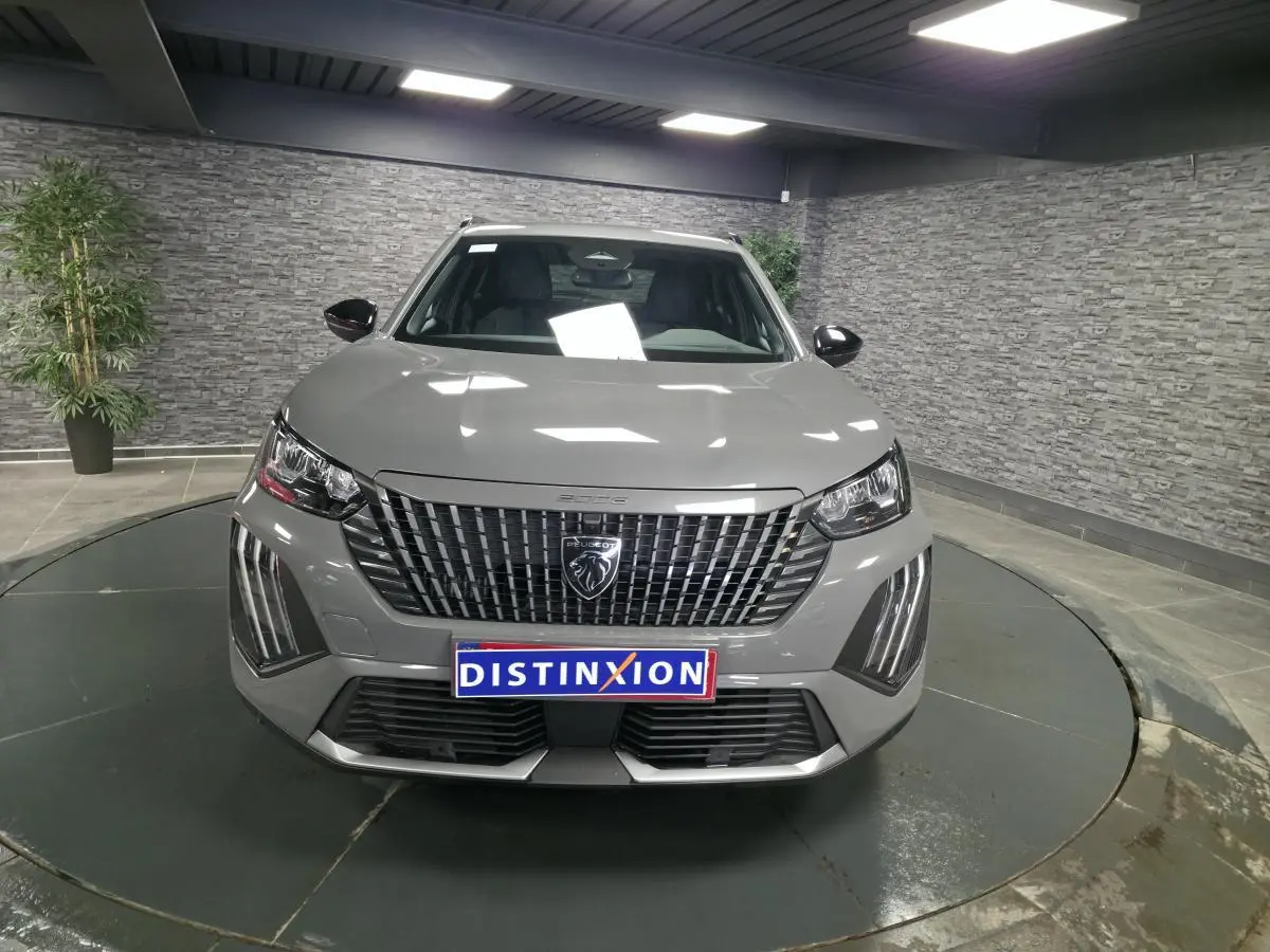 Vue frontale d'un Peugeot 2008 gris métallisé avec calandre verticale et feux LED en griffes, en intérieur showroom.