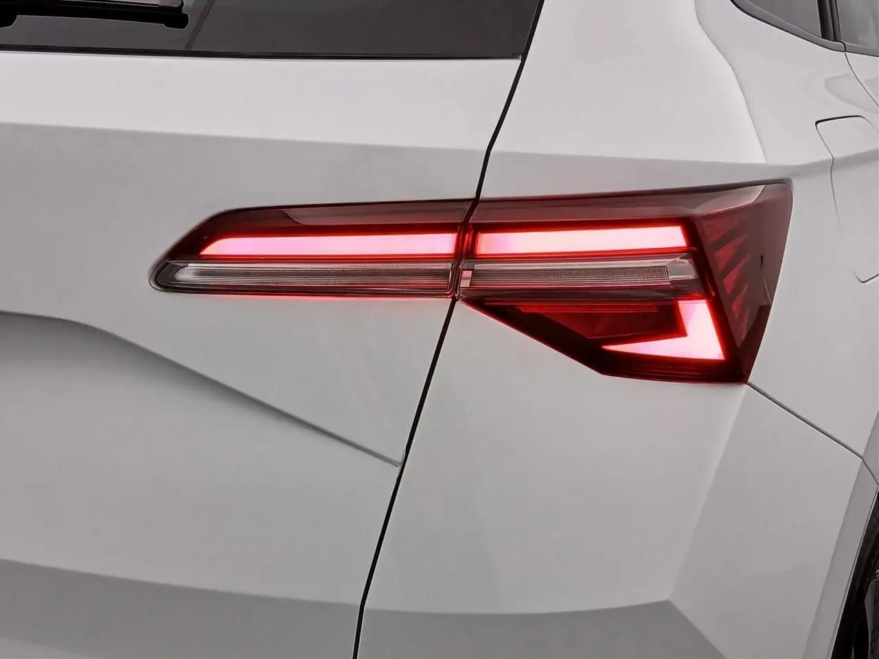Gros plan sur le feu arrière droit allumé d’un Skoda Karoq blanc lune, soulignant les lignes anguleuses du coffre.