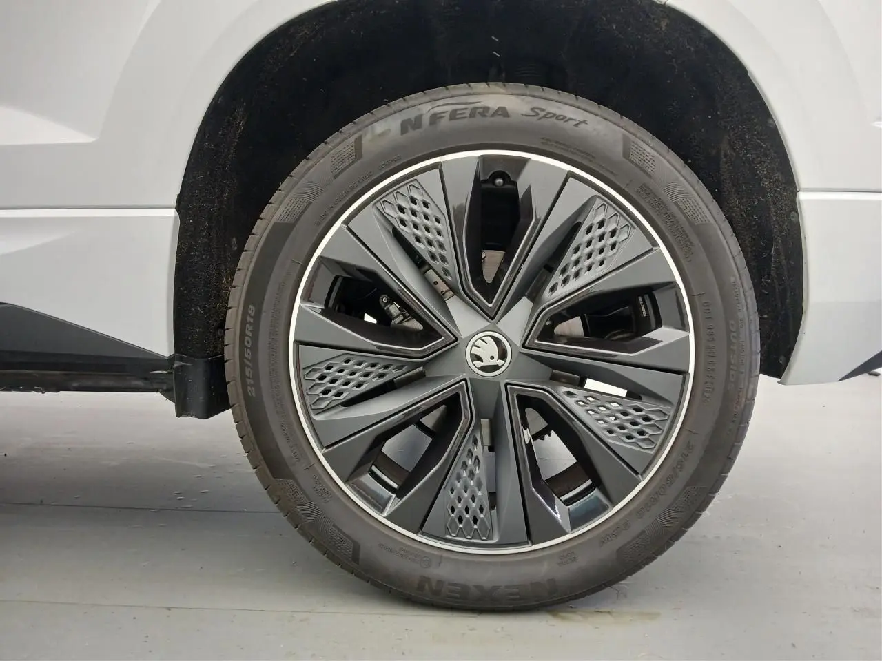 Gros plan sur la roue avant droite du Skoda Karoq blanc lune, mettant en valeur la jante design Sportline.