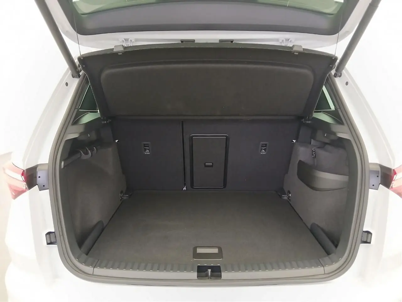 Coffre ouvert vu de l'arrière d'un Skoda Karoq blanc lune, montrant un espace de chargement spacieux et propre.