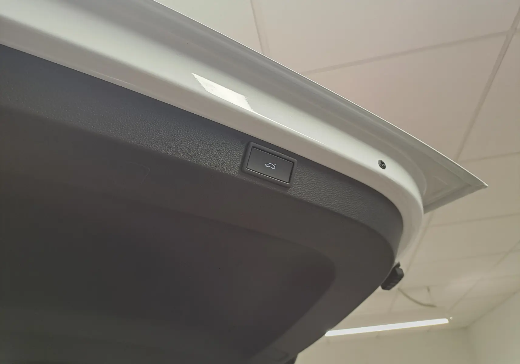 Bouton d'ouverture électrique du hayon sur la face intérieure du coffre d'un Skoda Karoq blanc lune.