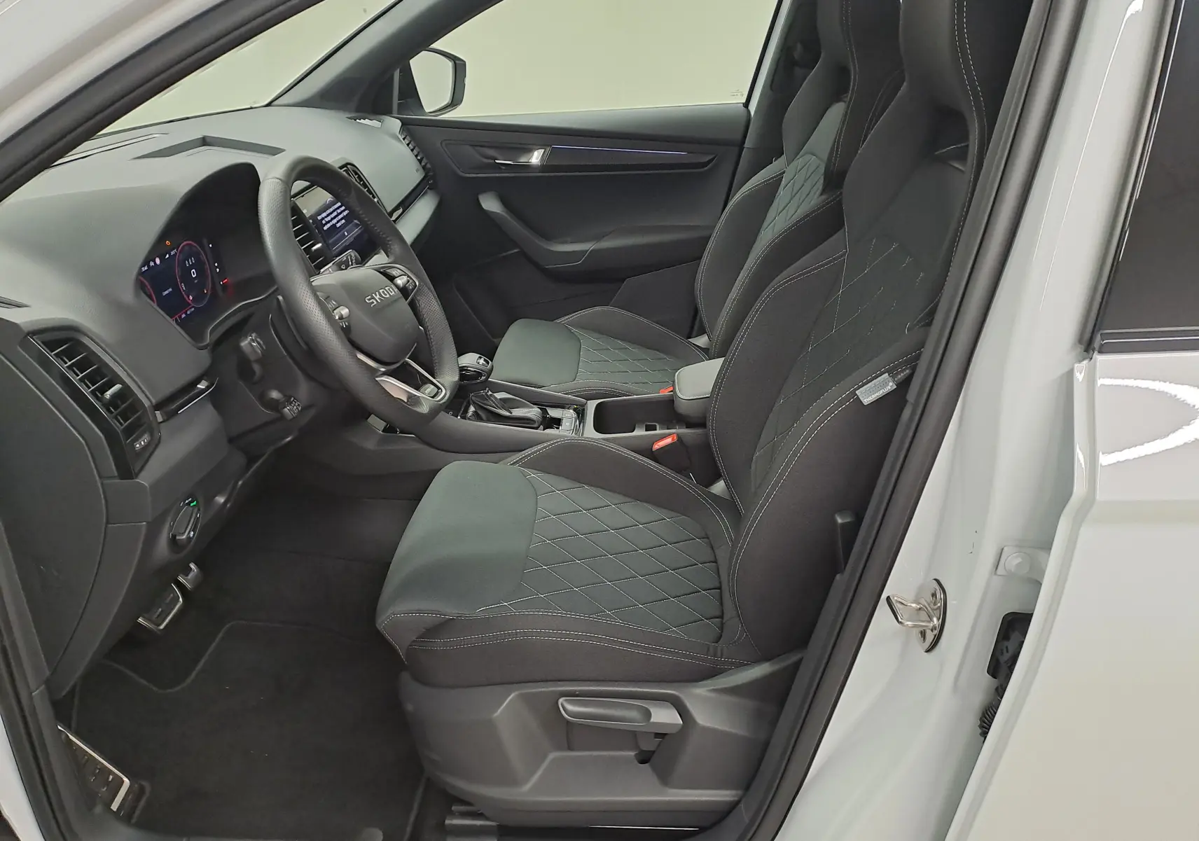 Vue intérieure côté conducteur du Skoda Karoq blanc lune 2025, sièges sport noirs avec surpiqûres contrastées.