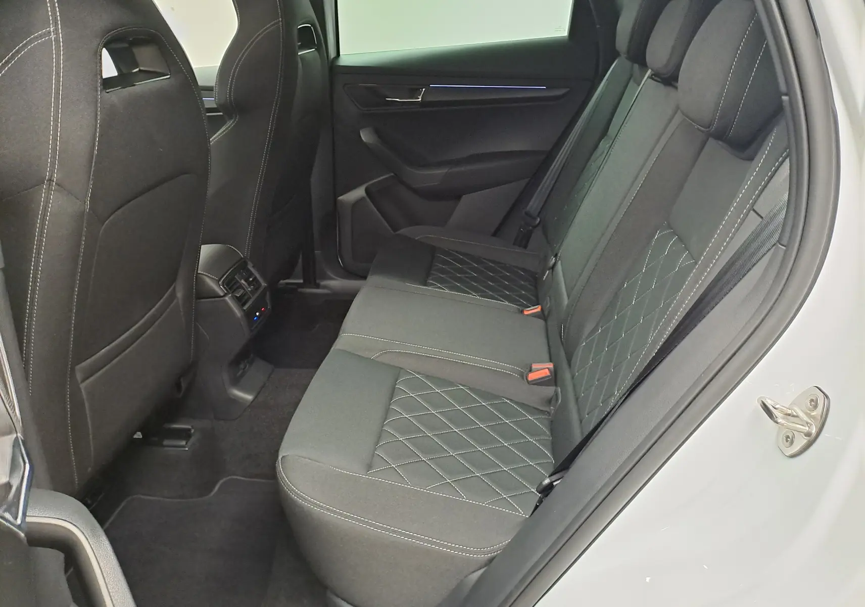 Vue intérieure côté droit des sièges arrière noirs avec surpiqûres blanches du Skoda Karoq blanc Lune 2025 Sportline.