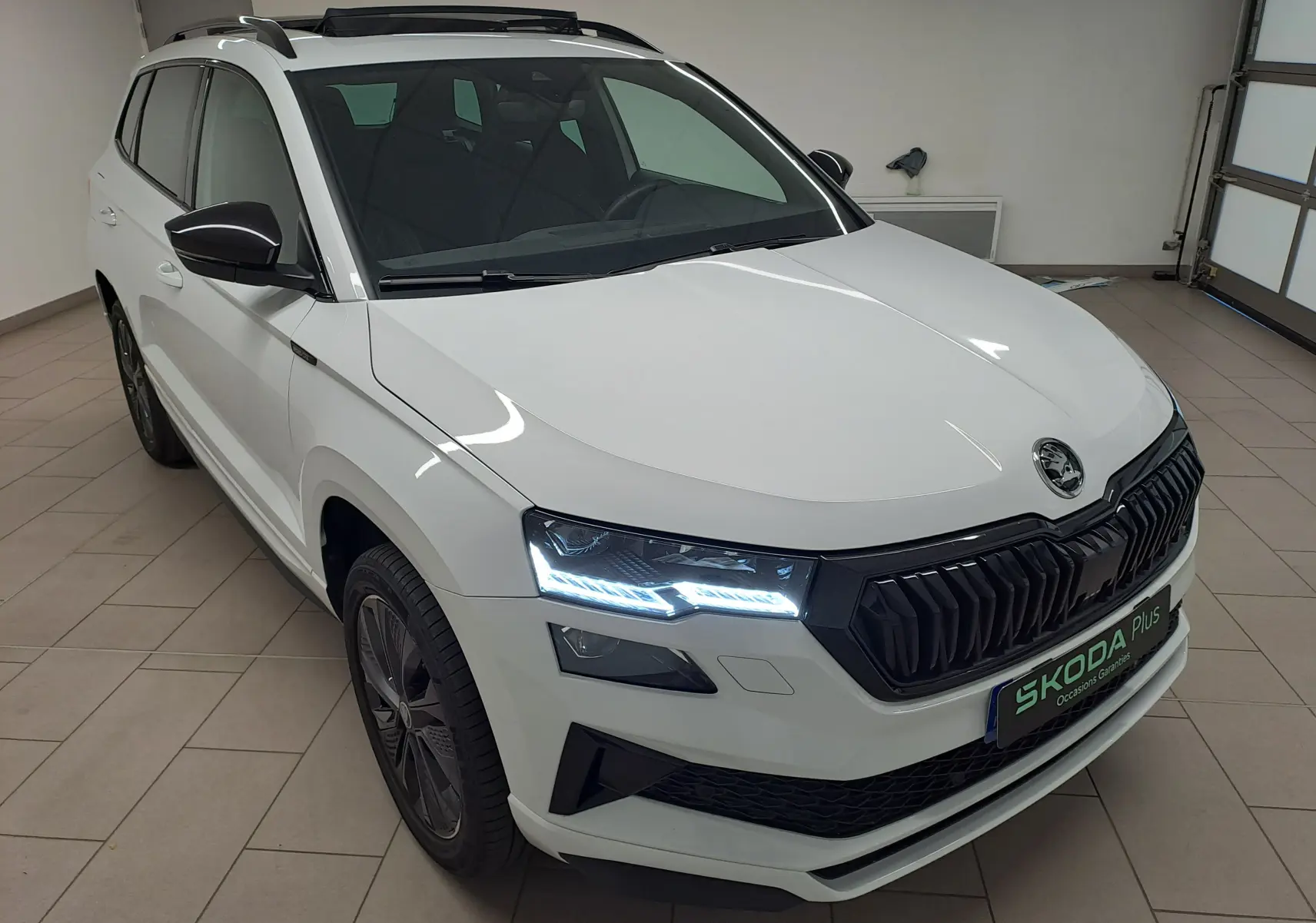 Vue 3/4 avant droit du Skoda Karoq blanc Lune avec phares LED allumés et calandre noire sportive.