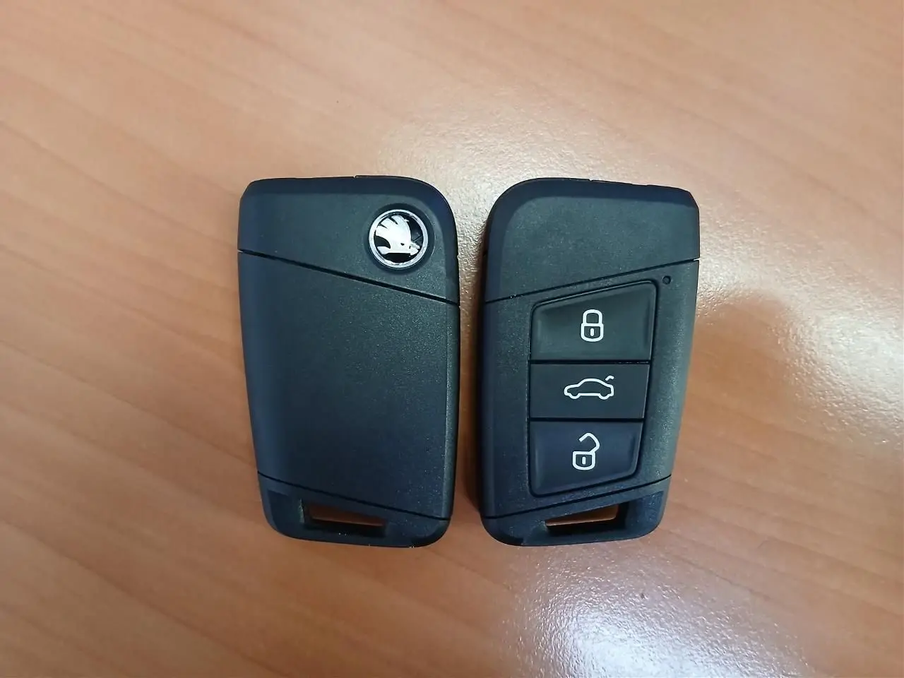 Deux clés noires de voiture Skoda posées sur une surface en bois, vues de face et de dos.