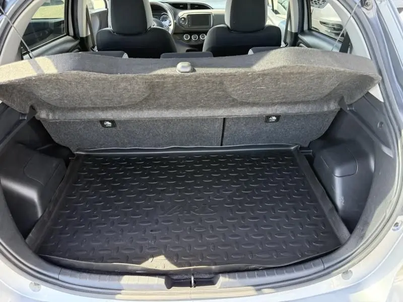 Coffre ouvert d'une Toyota Yaris gris métal 2020, vue arrière montrant le tapis de coffre et l'intérieur du véhicule.