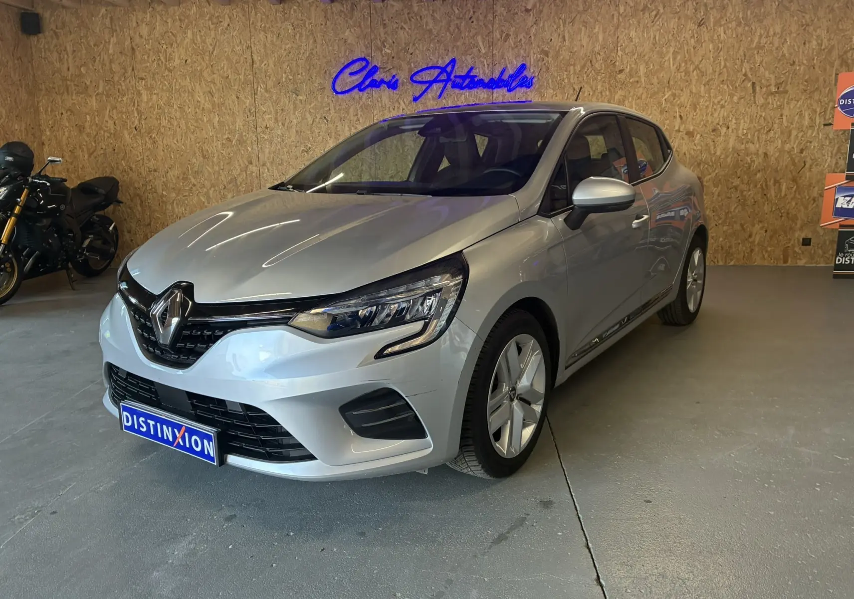 Renault Clio 1.5 BlueDCI Business gris vue 3/4 avant droit en intérieur avec logo Distinxion visible.