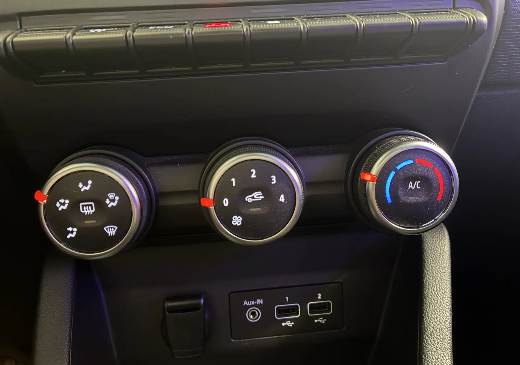 Gros plan sur les commandes de climatisation et ventilation d'une Renault Clio gris 2022, avec ports USB et prise auxiliaire visibles.