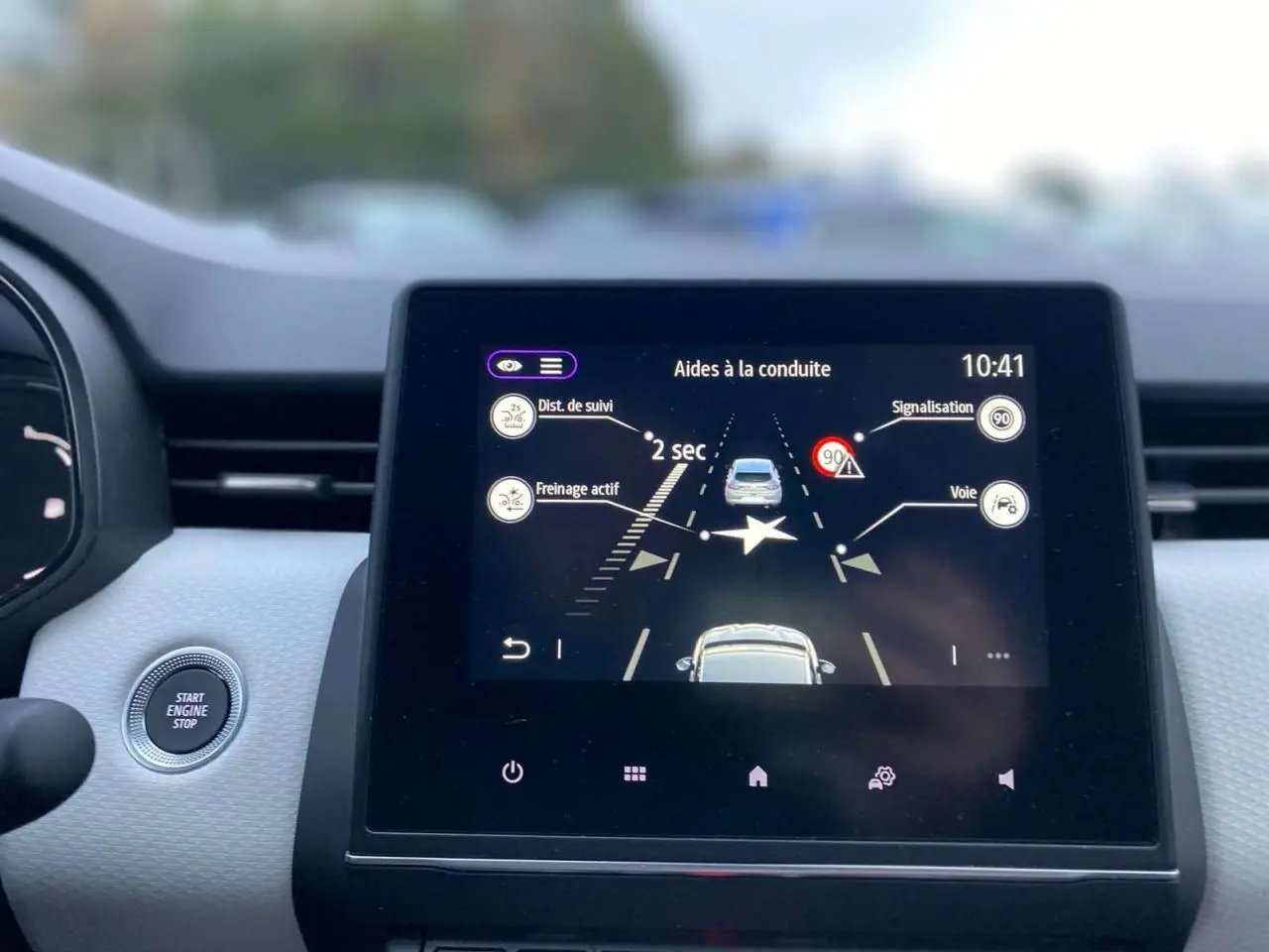 Écran tactile central de la Renault Clio 2023 affichant les aides à la conduite avec bouton démarrage visible à gauche.