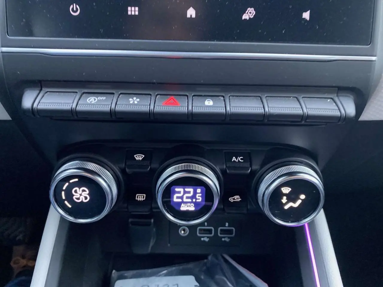 Gros plan sur la console centrale de la Renault Clio blanche 2023, montrant les commandes de climatisation automatique et ports USB.