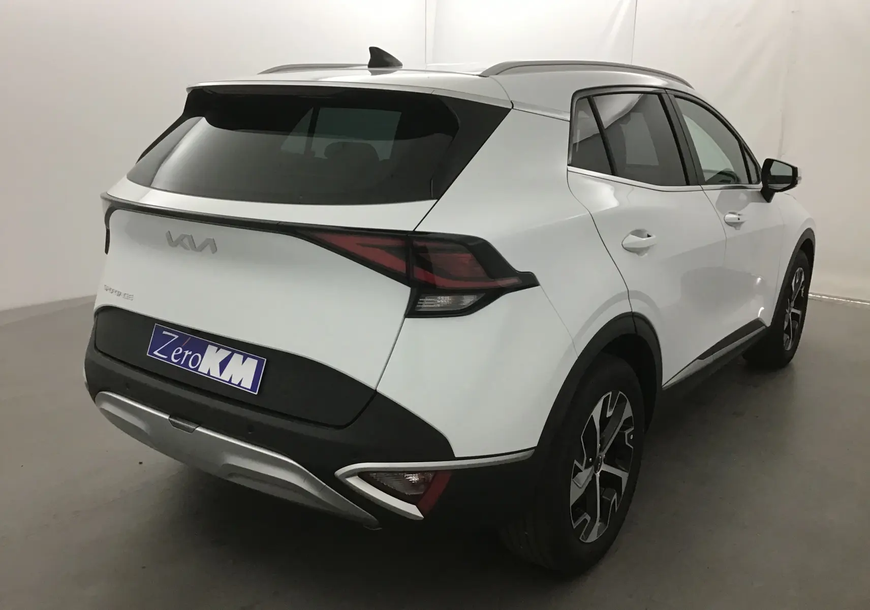 Vue 3/4 arrière droite du KIA SPORTAGE blanc 2025 avec feux arrière LED et jantes alliage noires et argentées.