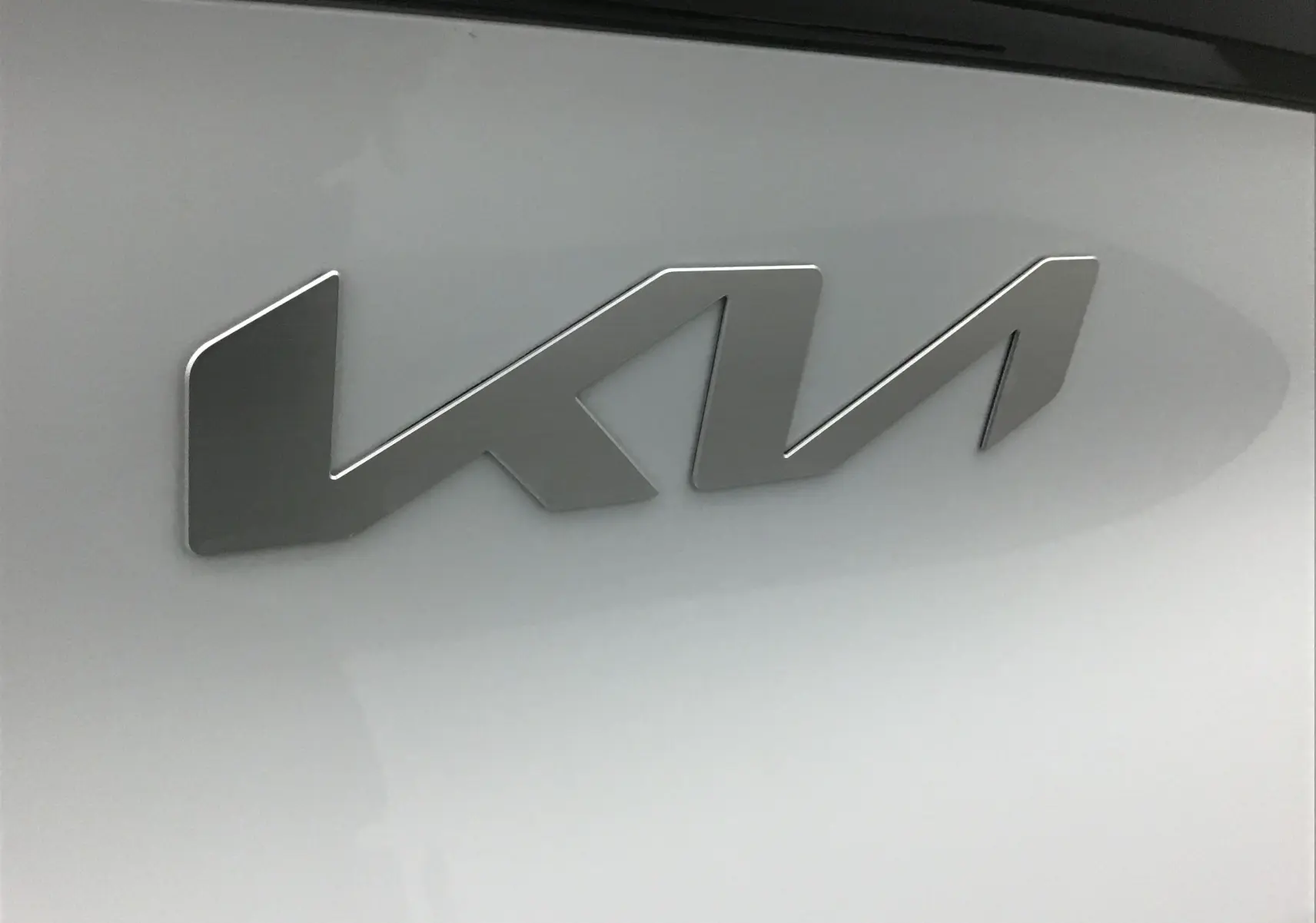 Gros plan sur l'emblème KIA en métal brossé sur la carrosserie blanche du SUV Sportage 2025.