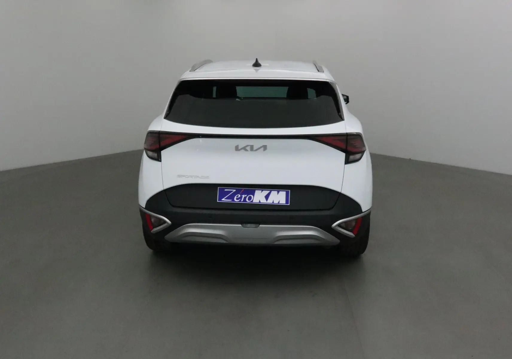 Vue arrière d'un Kia Sportage blanc 2025 avec feux arrière en bandeau et plaque Zero KM.