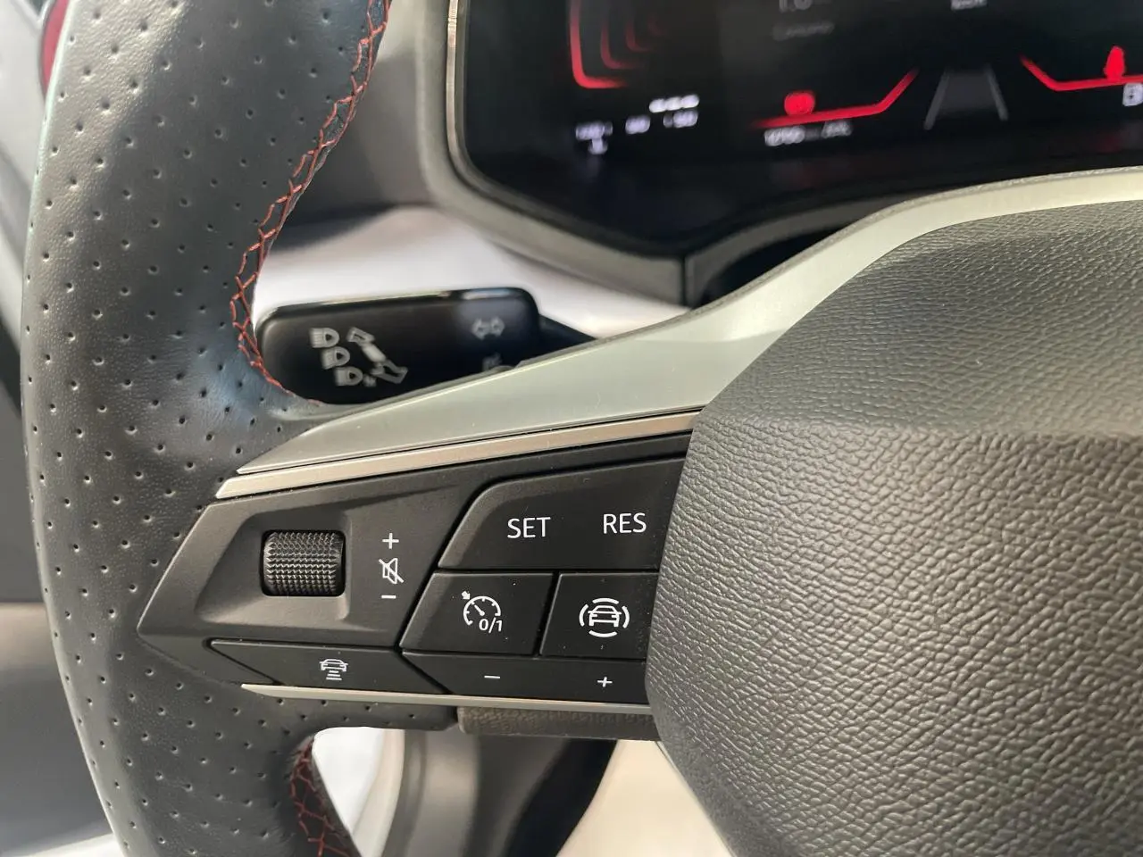 Gros plan sur le volant cuir noir perforé avec surpiqûres rouges du SEAT Arona 2024, boutons de régulateur de vitesse visibles.