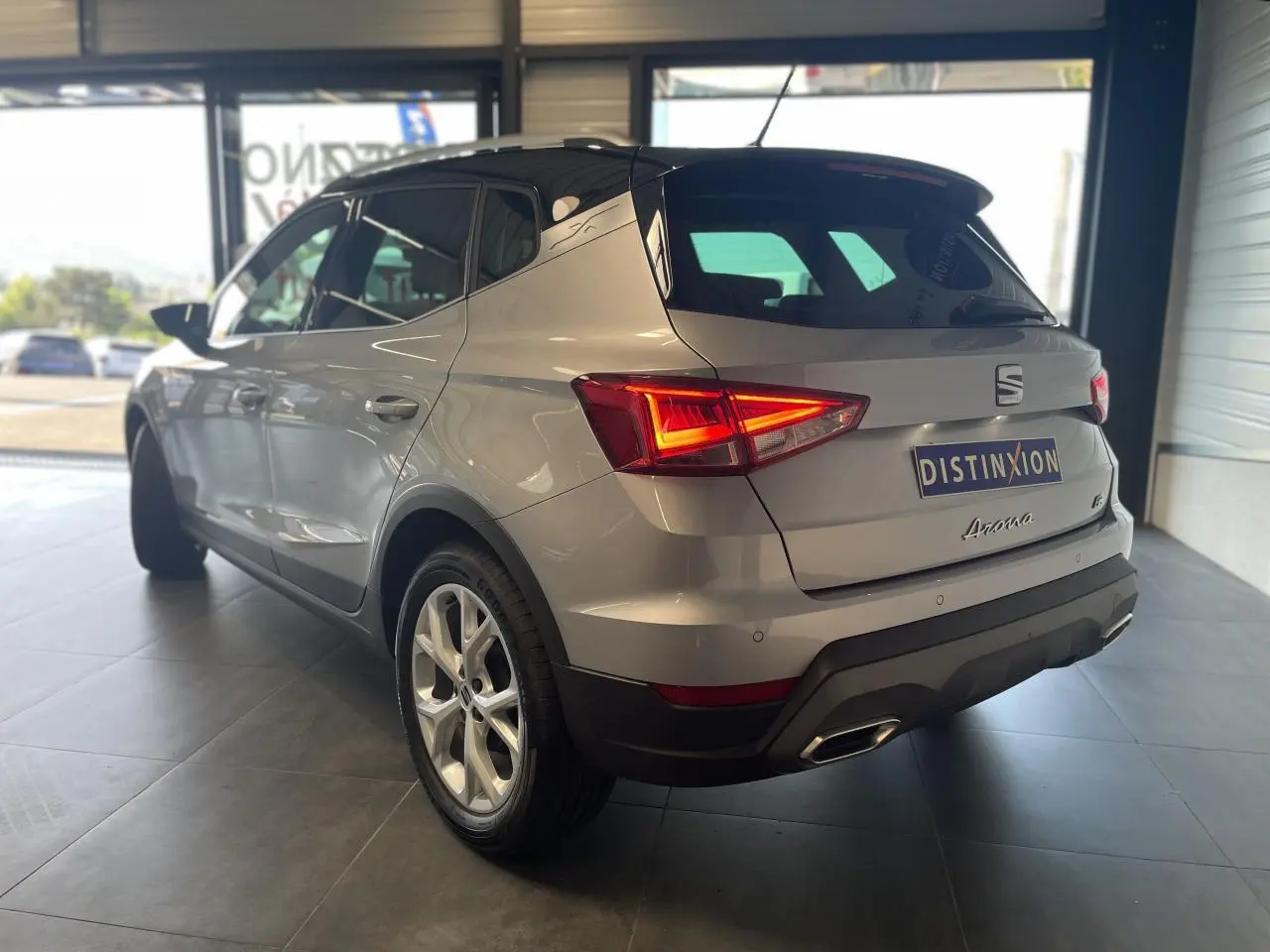 Vue 3/4 arrière droite d'une SEAT Arona 2024 rouge passion avec feux arrière allumés en showroom.