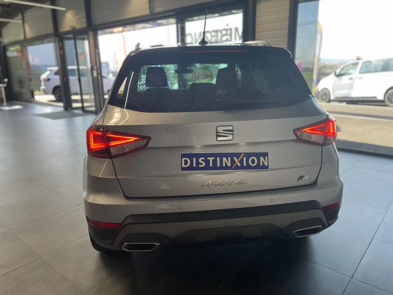 Vue arrière d'un SEAT Arona 1.0 TSI FR gris GRS avec feux allumés et double sortie d'échappement chromée.