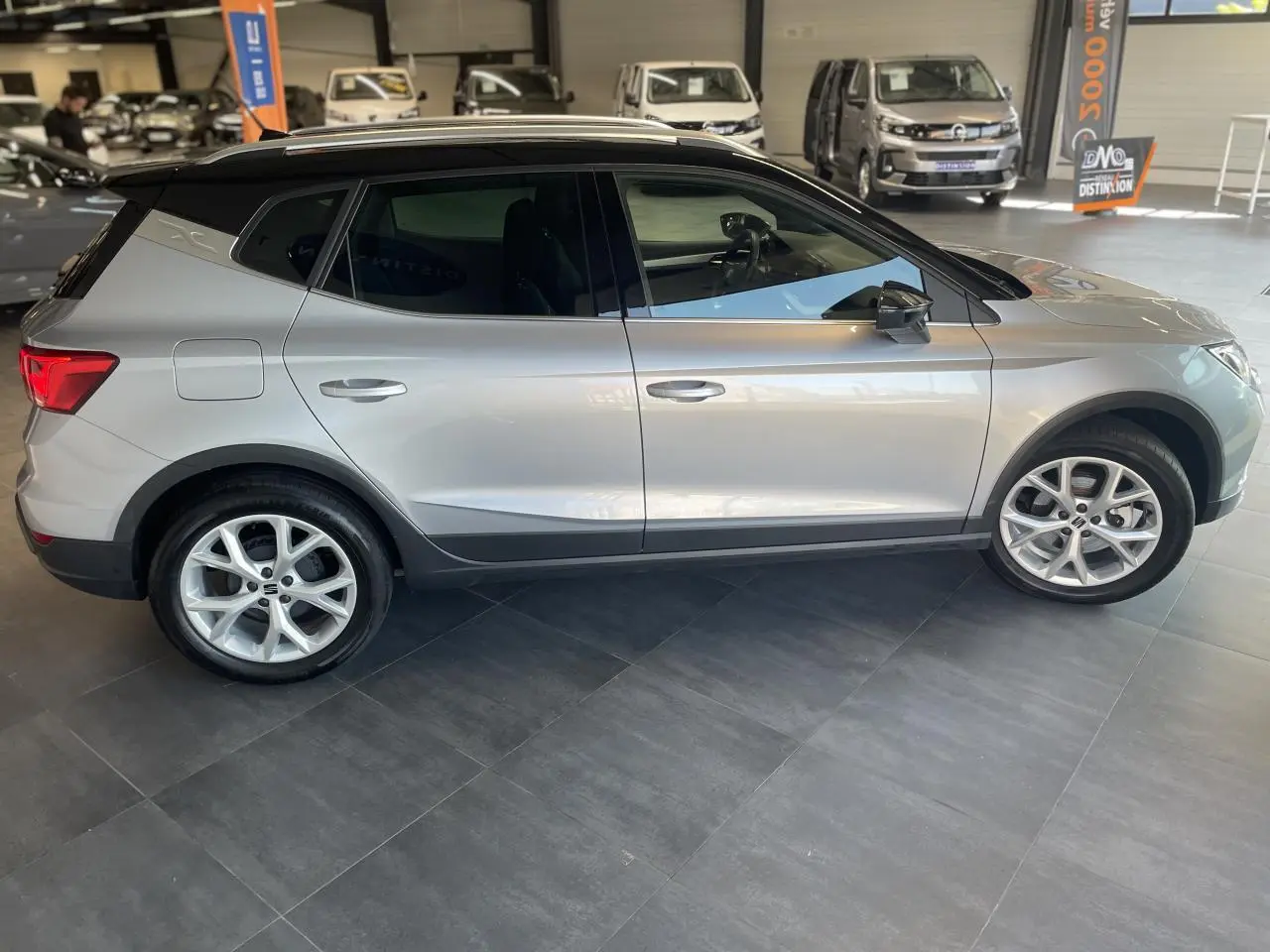 SEAT Arona 2024 gris clair vue de profil côté gauche, avec toit noir et jantes alliage 16 pouces en showroom.