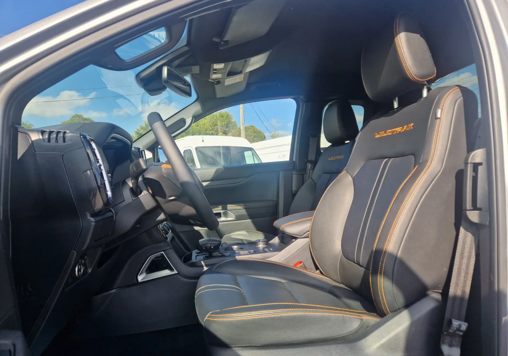Vue intérieure côté conducteur du Ford Ranger Super Cabine Wildtrak 2025, sièges cuir noirs avec surpiqûres orange et logo brodé.