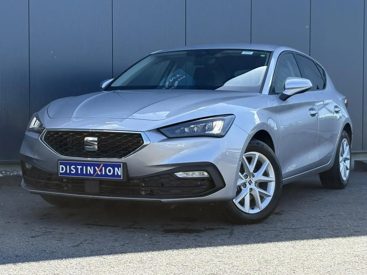 SEAT Leon gris argent vue 3/4 avant droit, jantes alliage 16 pouces et calandre hexagonale distinctive.