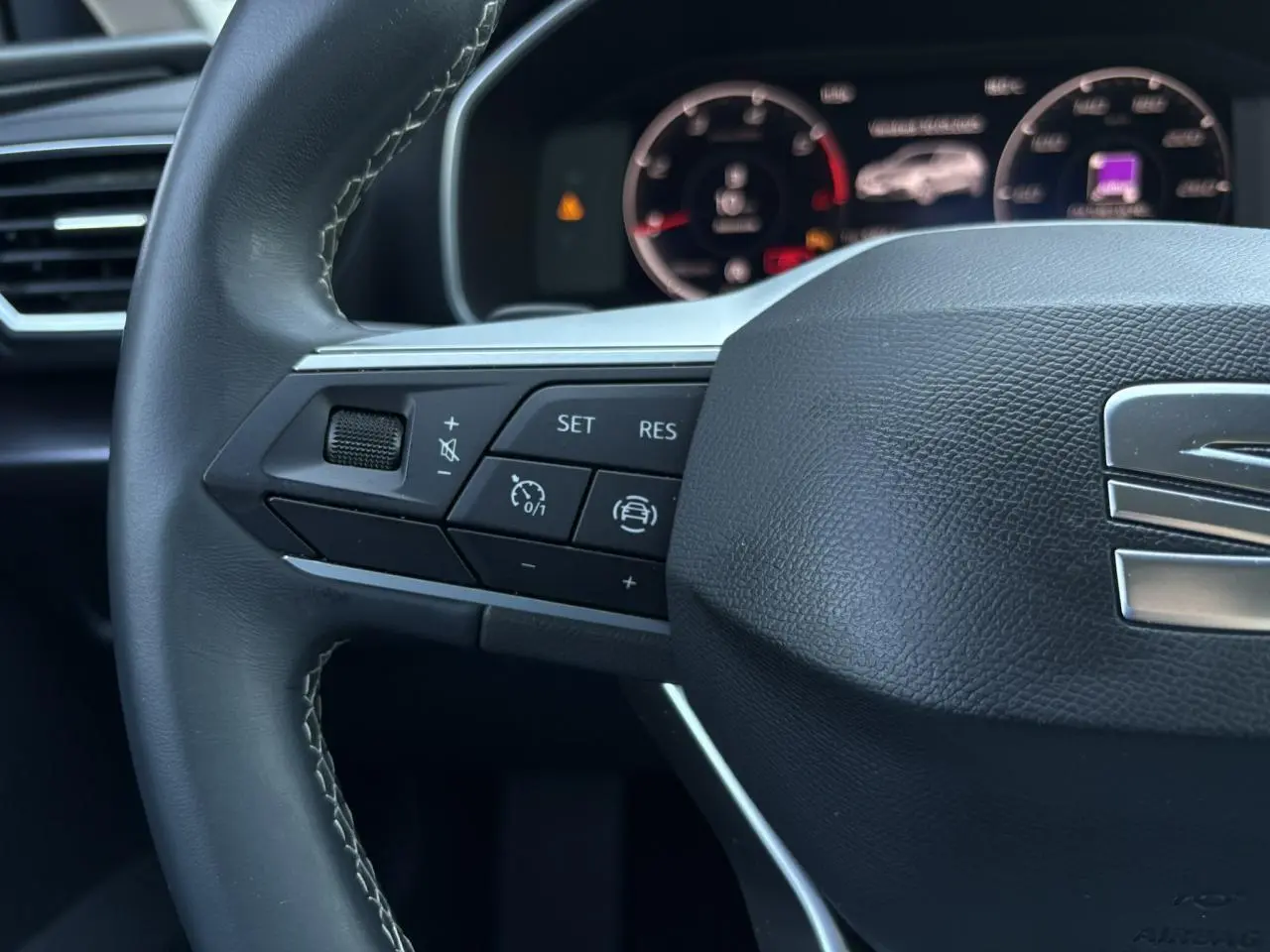 Gros plan sur le volant cuir multifonction gris foncé du SEAT Leon 2024 avec commandes de régulateur et affichage digital en arrière-plan.