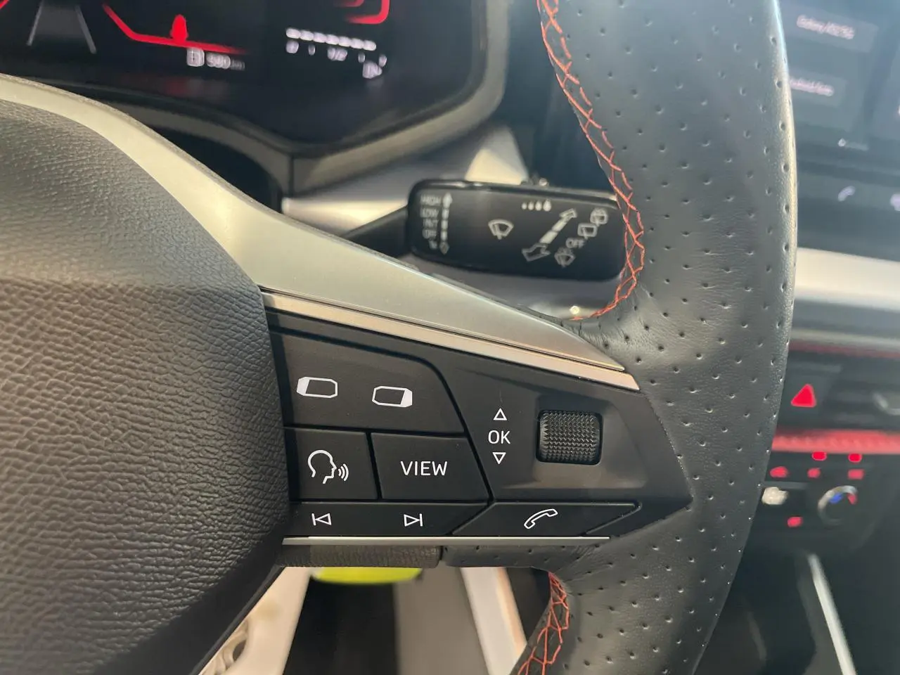 Gros plan sur le volant cuir perforé noir avec surpiqûres rouges du SEAT Arona 2024, boutons multifonctions visibles.