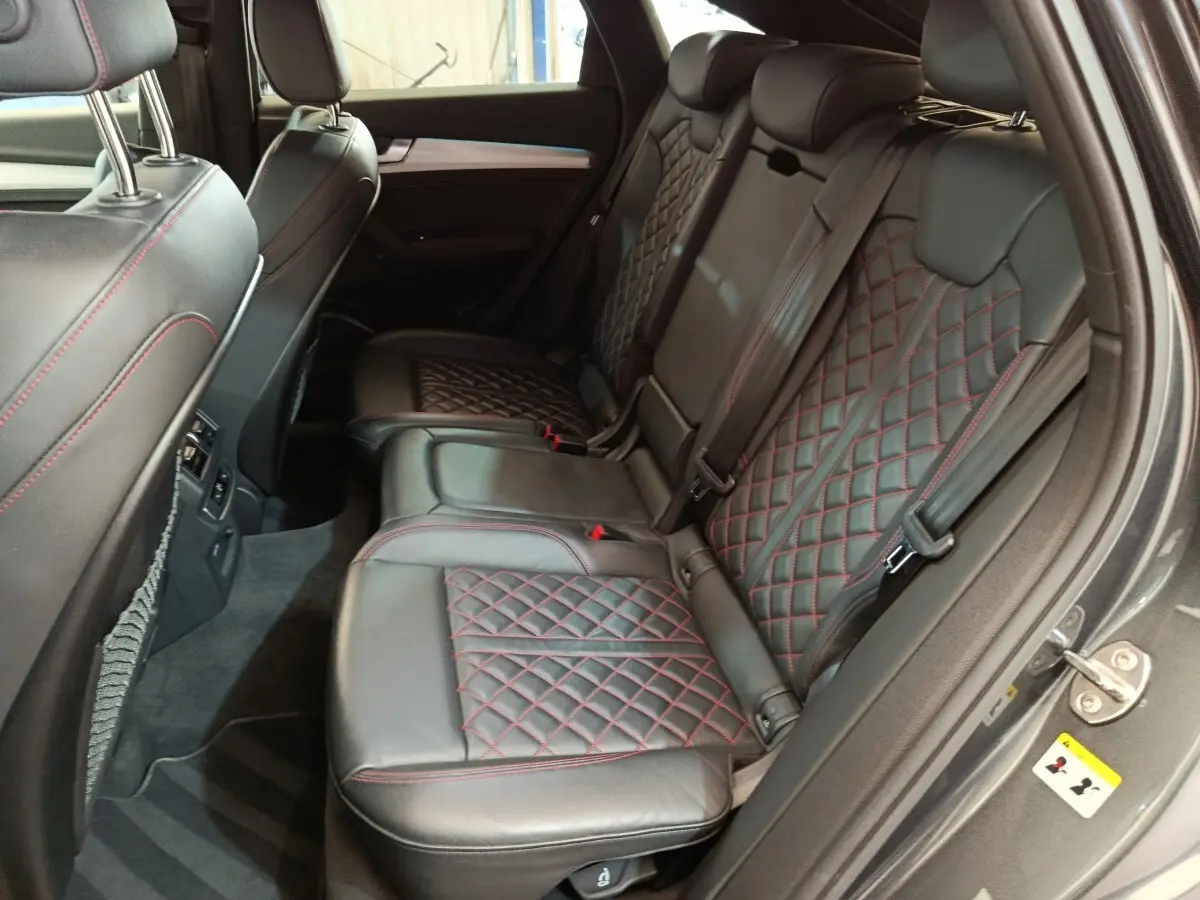 Vue intérieure côté droit des sièges arrière en cuir noir avec surpiqûres rouges de l'Audi Q5 gris clair 2023 hybride rechargeable.