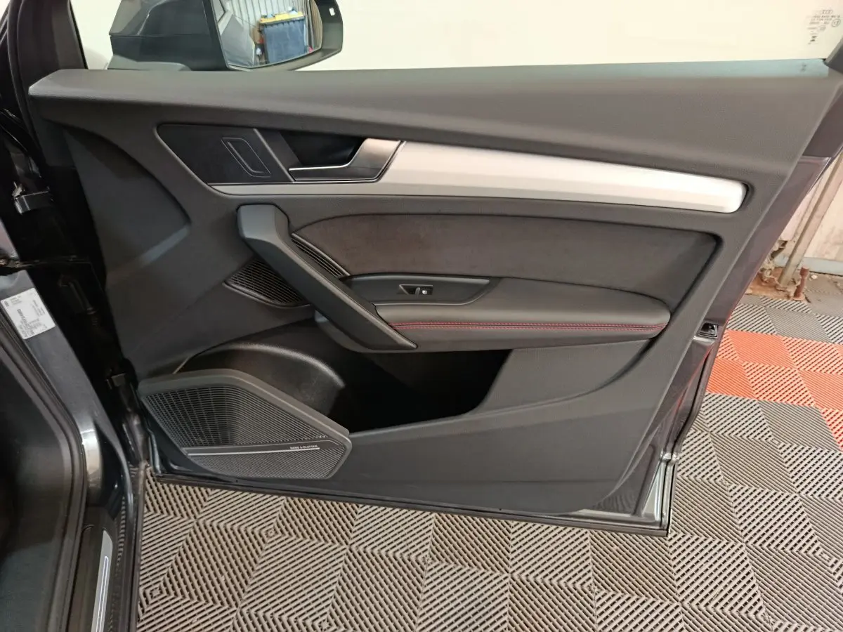 Vue rapprochée de la porte avant gauche d’un Audi Q5 gris clair 2023, avec garniture noire et surpiqûres rouges.