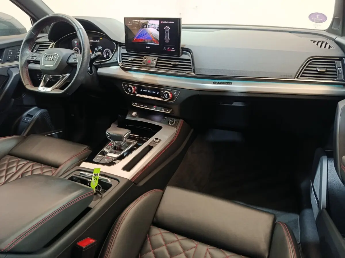 Vue intérieure de l'Audi Q5 2023 hybride rechargeable, montrant le tableau de bord, volant et console centrale en cuir noir avec surpiqûres rouges.