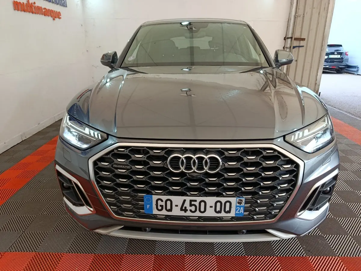 Vue avant d’un Audi Q5 gris clair 2023 hybride rechargeable, mettant en valeur sa calandre hexagonale et ses phares LED allumés.
