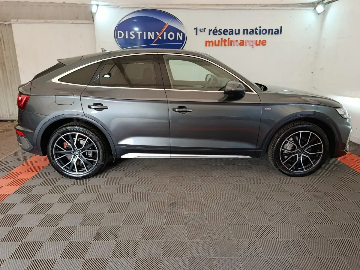 Vue de profil côté droit d'un Audi Q5 gris clair hybride rechargeable 2023 avec jantes noires sport et toit incliné.
