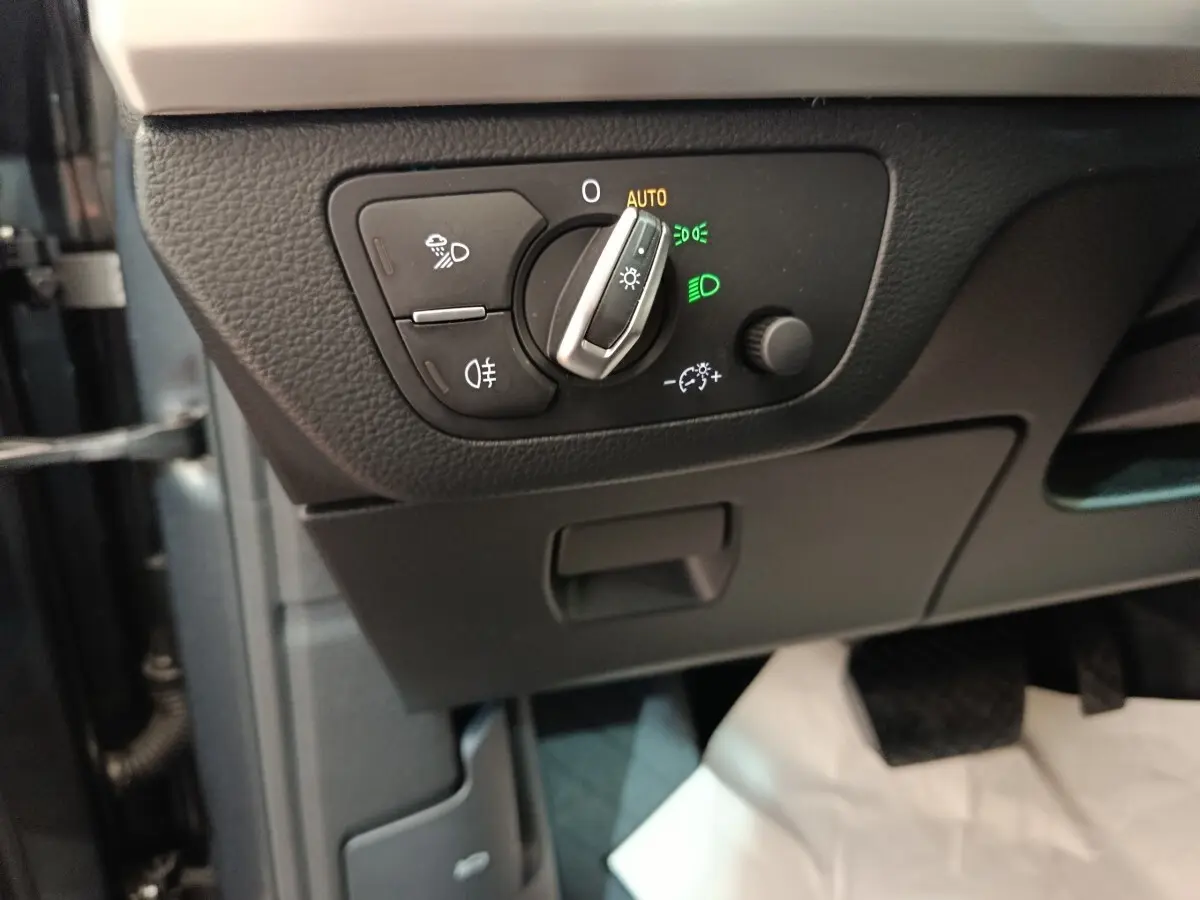 Gros plan sur le bouton de commande des phares avec réglage automatique dans l'Audi Q5 gris clair 2023 hybride rechargeable.