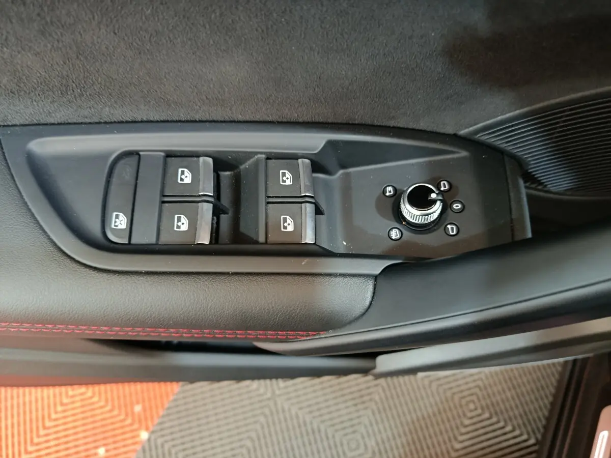 Gros plan sur les commandes de lève-vitres et réglage des rétroviseurs côté conducteur d’un Audi Q5 gris clair 2023.