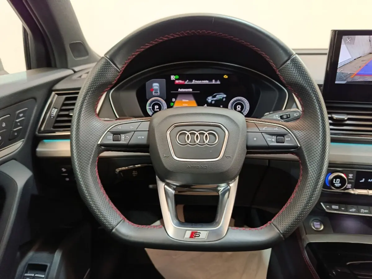 Vue centrée sur le volant perforé avec surpiqûres rouges de l'Audi Q5 2023 hybride rechargeable, tableau de bord digital visible.