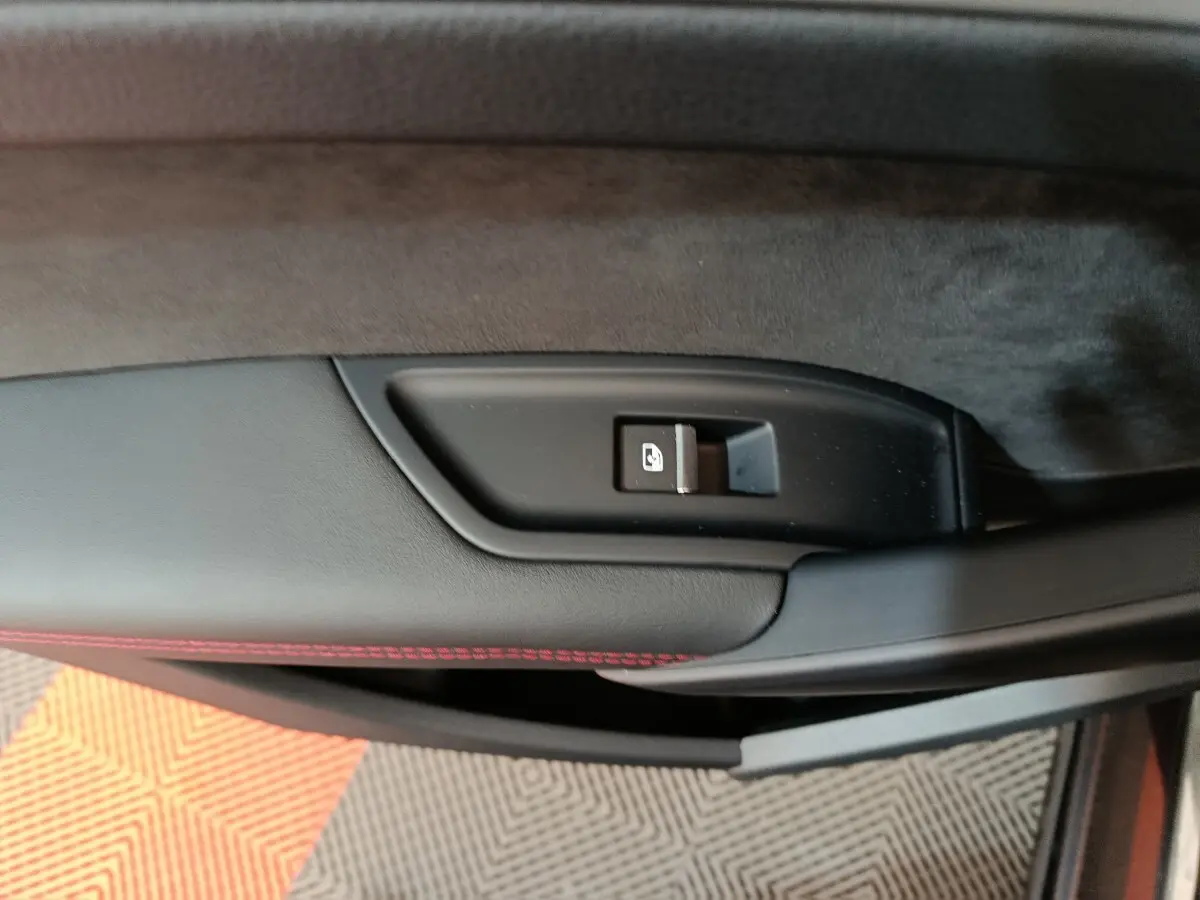 Gros plan sur la commande de verrouillage de porte côté gauche d’un Audi Q5 2023 gris clair avec surpiqûres rouges.