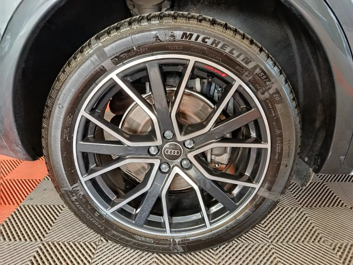 Gros plan sur la roue avant droite d’un Audi Q5 gris clair 2023 avec jante alliage noir et logo Audi au centre.