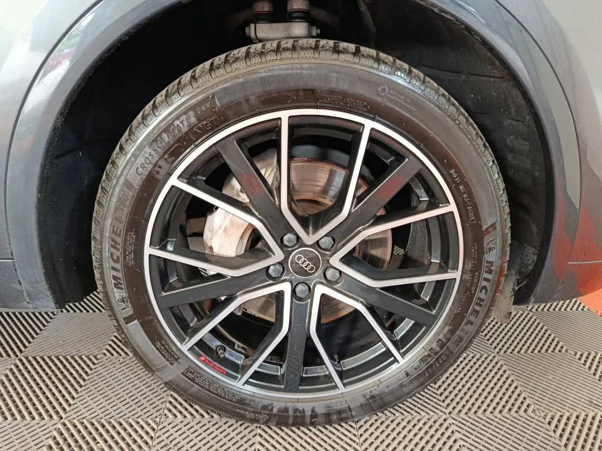 Gros plan sur la roue avant droite d’un Audi Q5 gris clair 2023, jante noire à branches fines avec logo Audi au centre.