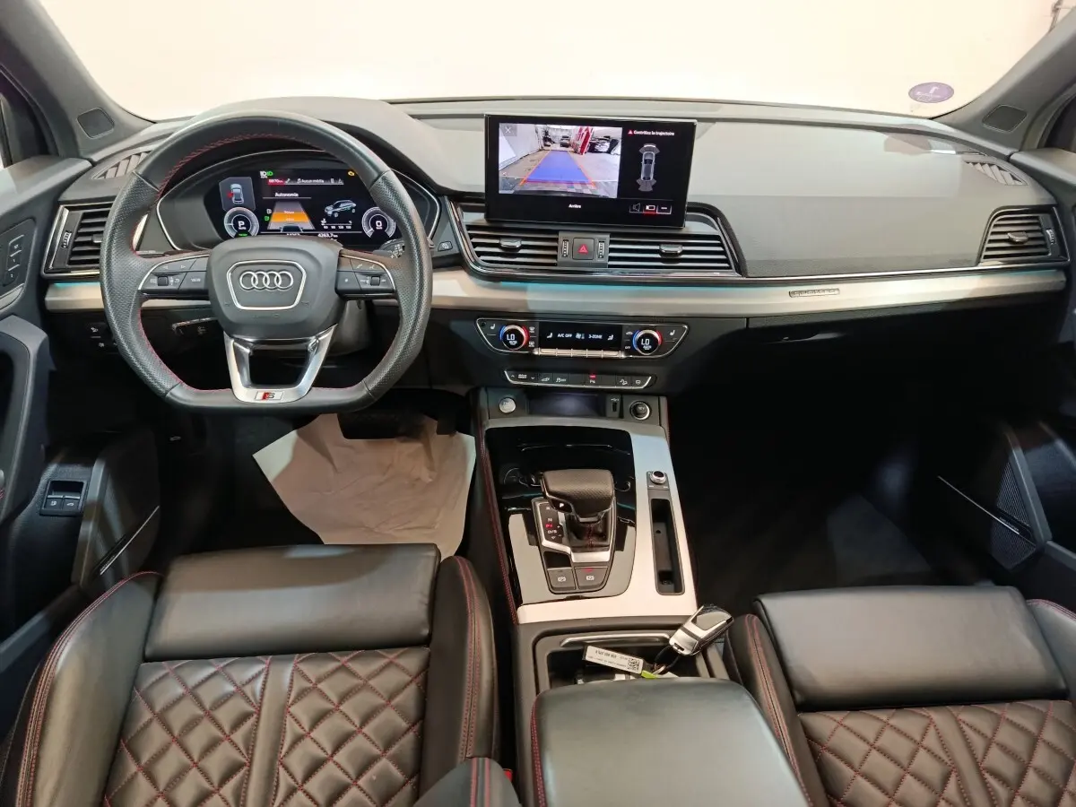 Vue intérieure avant de l'Audi Q5 2023 hybride rechargeable, avec tableau de bord moderne et sièges en cuir noir surpiqués rouges.