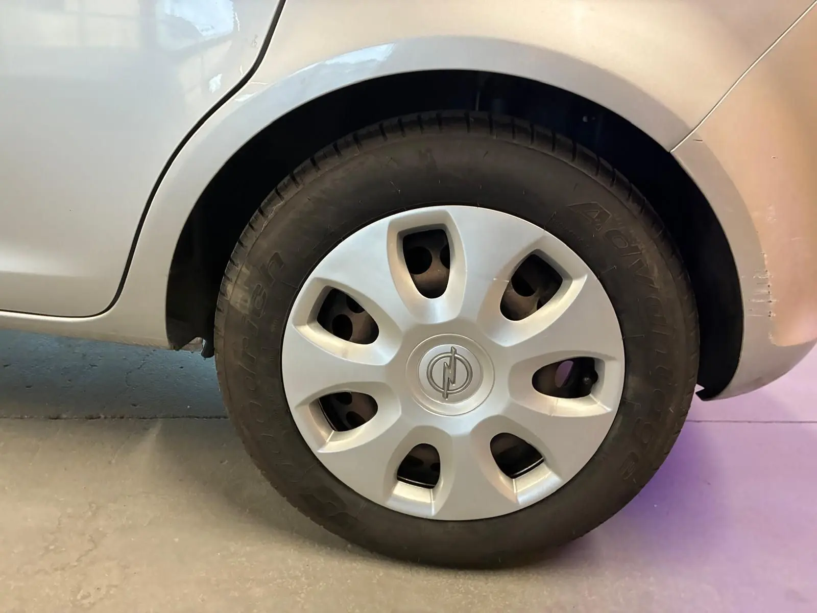 Gros plan sur la roue avant droite grise claire d'une Opel Corsa 1.2i 85 Edition de 2012 avec enjoliveur Opel.