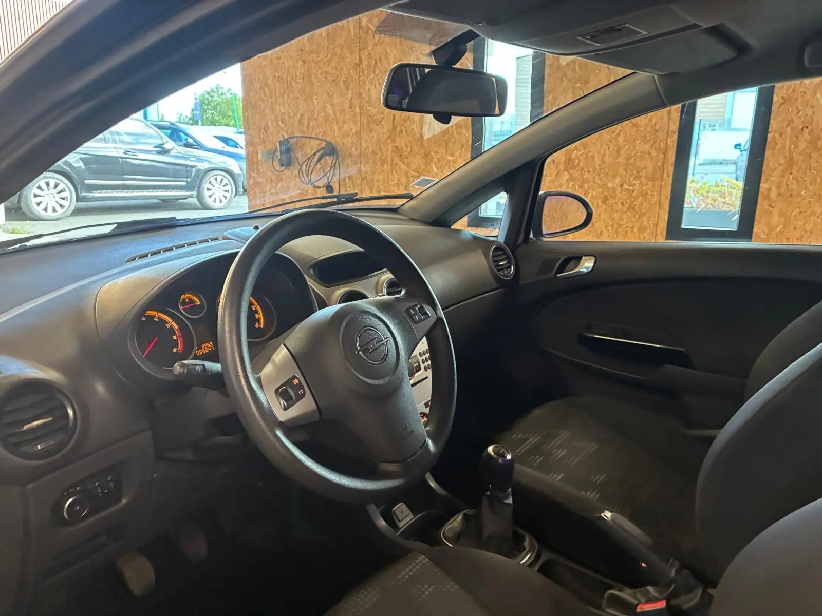 Vue intérieure côté conducteur de l’Opel Corsa gris clair 2012, volant multifonction et sellerie tissu noir visibles.
