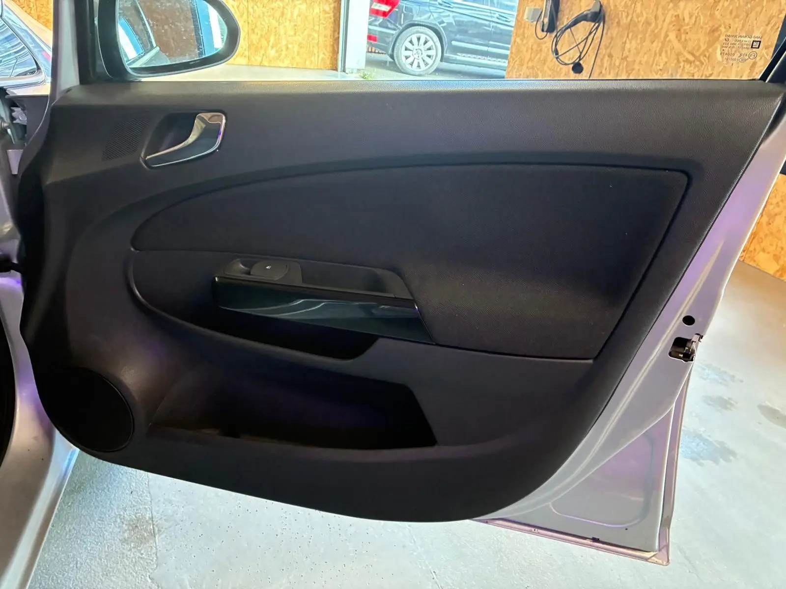 Vue intérieure de la porte avant gauche d’une Opel Corsa gris clair 2012 avec garniture noire et poignée argentée.