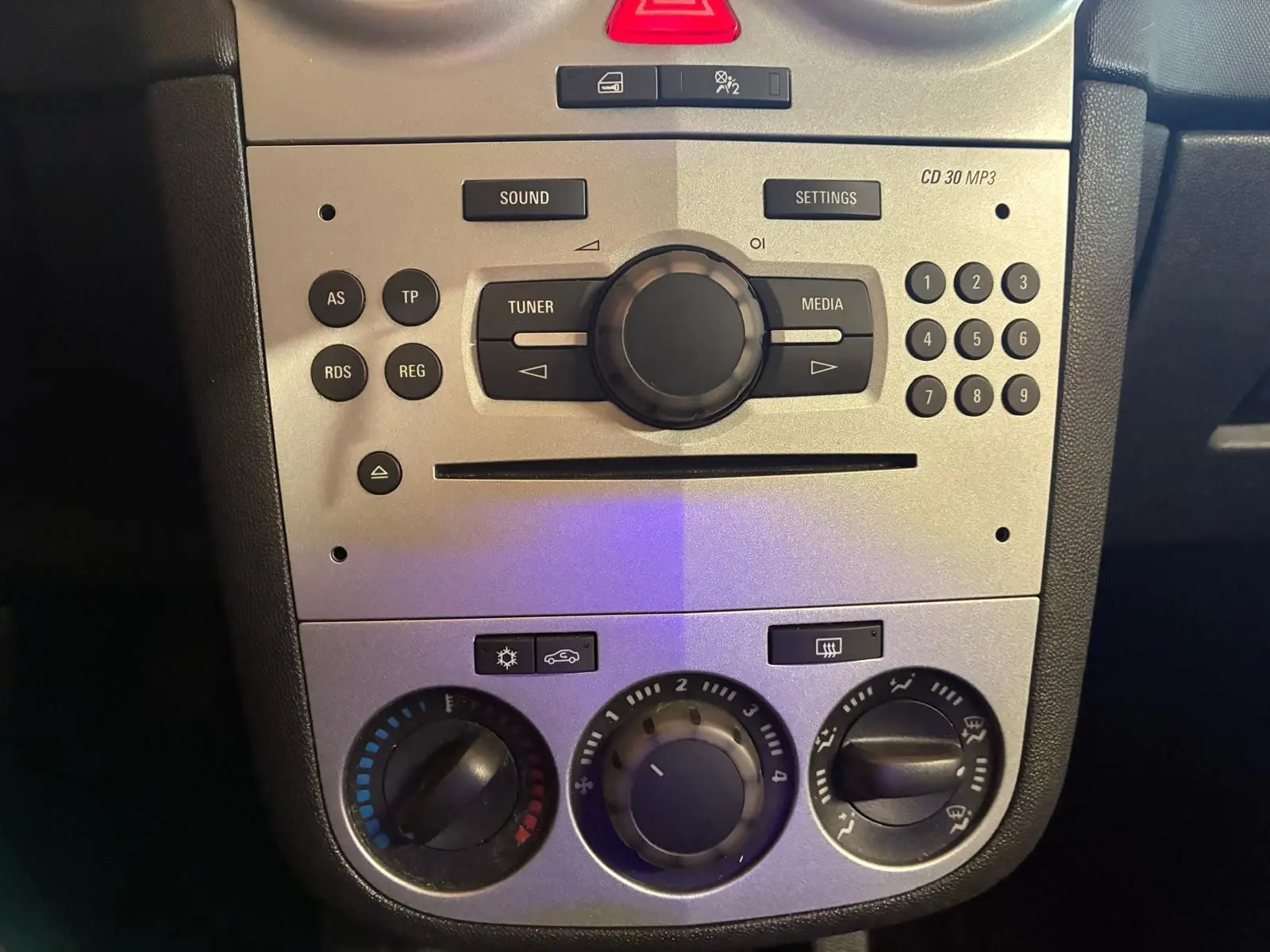 Vue rapprochée du tableau de bord gris clair de l’Opel Corsa 2012 avec commandes radio et climatisation manuelle.