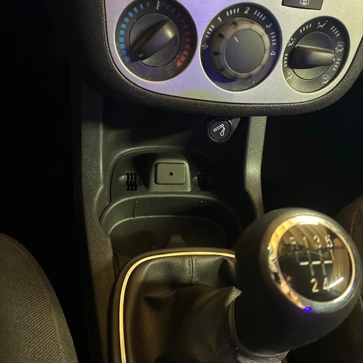Gros plan sur la console centrale d'une Opel Corsa gris clair 2012, avec levier de vitesse manuel et commandes de climatisation.