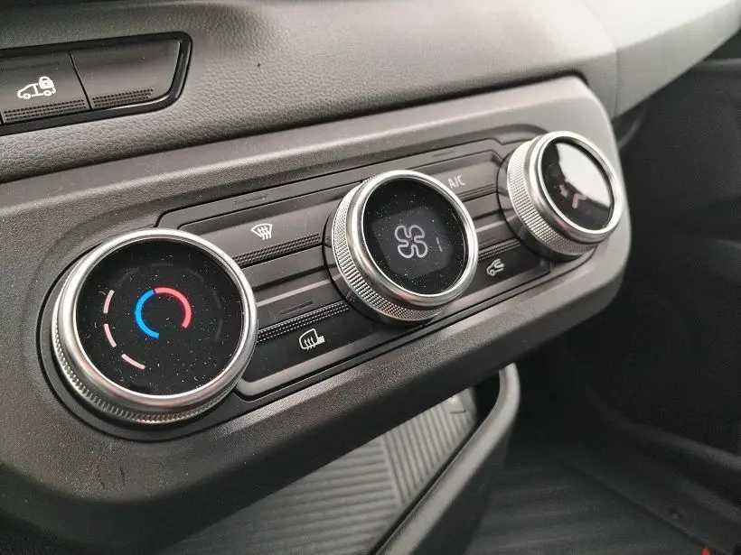 Gros plan sur les commandes de climatisation du Nissan Interstar Fourgon blanc, avec réglages circulaires argentés et tableau de bord noir.