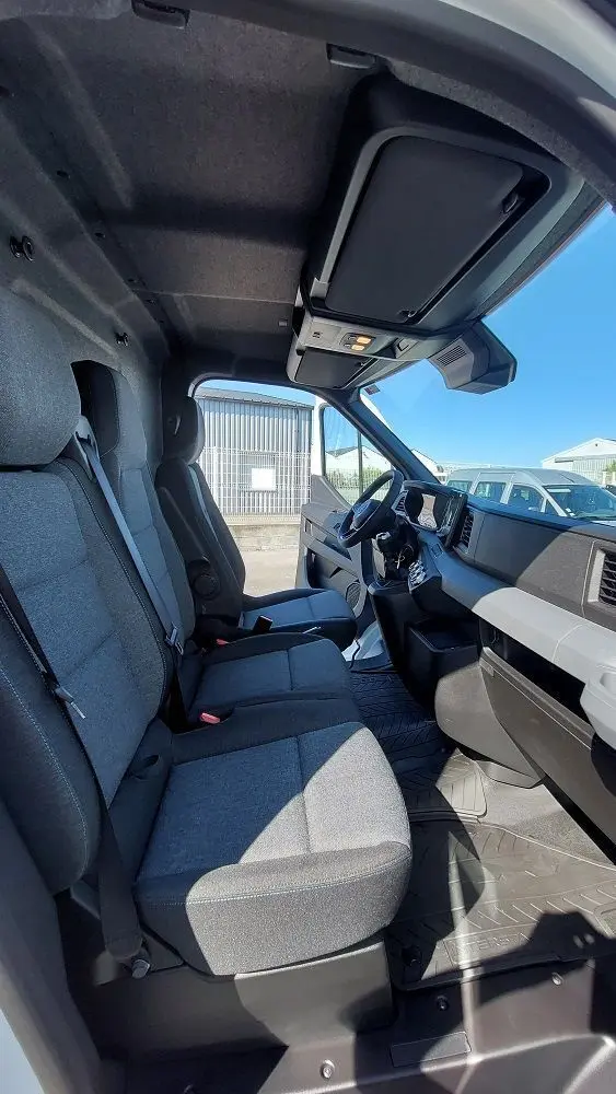 Vue intérieure côté conducteur du Nissan Interstar Fourgon 2025, sièges gris et tableau de bord moderne sous lumière naturelle.