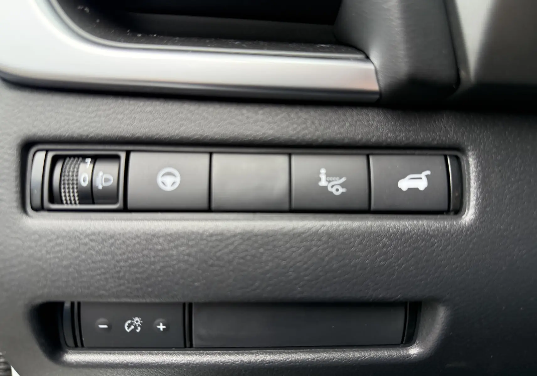 Gros plan sur les commandes noires du tableau de bord du Nissan Qashqai blanc nacré, avec boutons de réglage et ouverture du coffre.